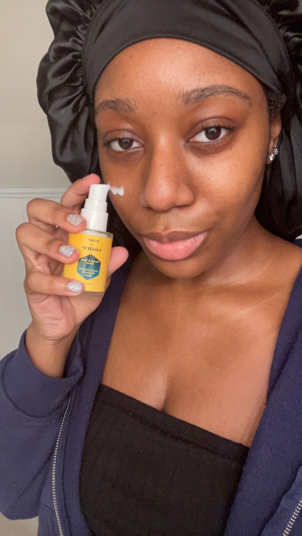Model with melanin-rich skin holding VOUEE NÜWR Dark spot serum for removing dark spots from darker skin tones.